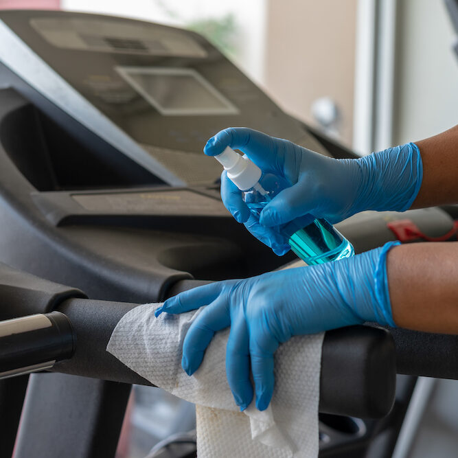 Staff using wet wipe and a blue sanitizer from the bottle to clean treadmill in gym. Antiseptic,disinfection ,cleanliness and healthcare, Anti Corona virus (COVID-19).